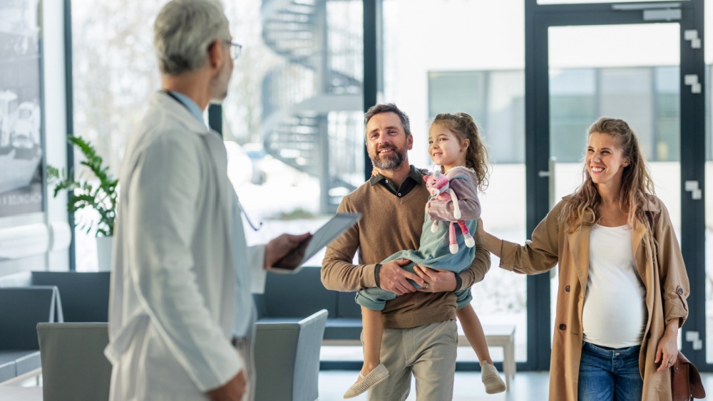 man carrying a little girl and pregnant woman meet doctor
